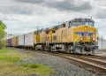 yellow and black train on rail tracks under white clouds and blue sky during daytime