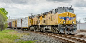 yellow and black train on rail tracks under white clouds and blue sky during daytime