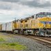 yellow and black train on rail tracks under white clouds and blue sky during daytime